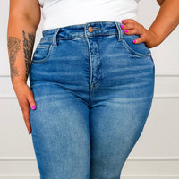 Curvy model wearing Risen Tummy Control jeans standing on a wooden floor with a white paneled wall in the background