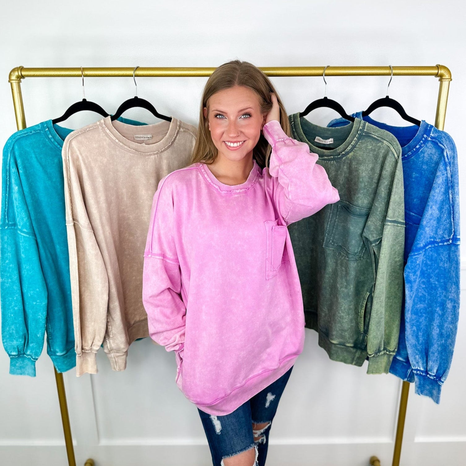 Woman in a pink sweatshirt standing next to a rack of colorful sweaters.