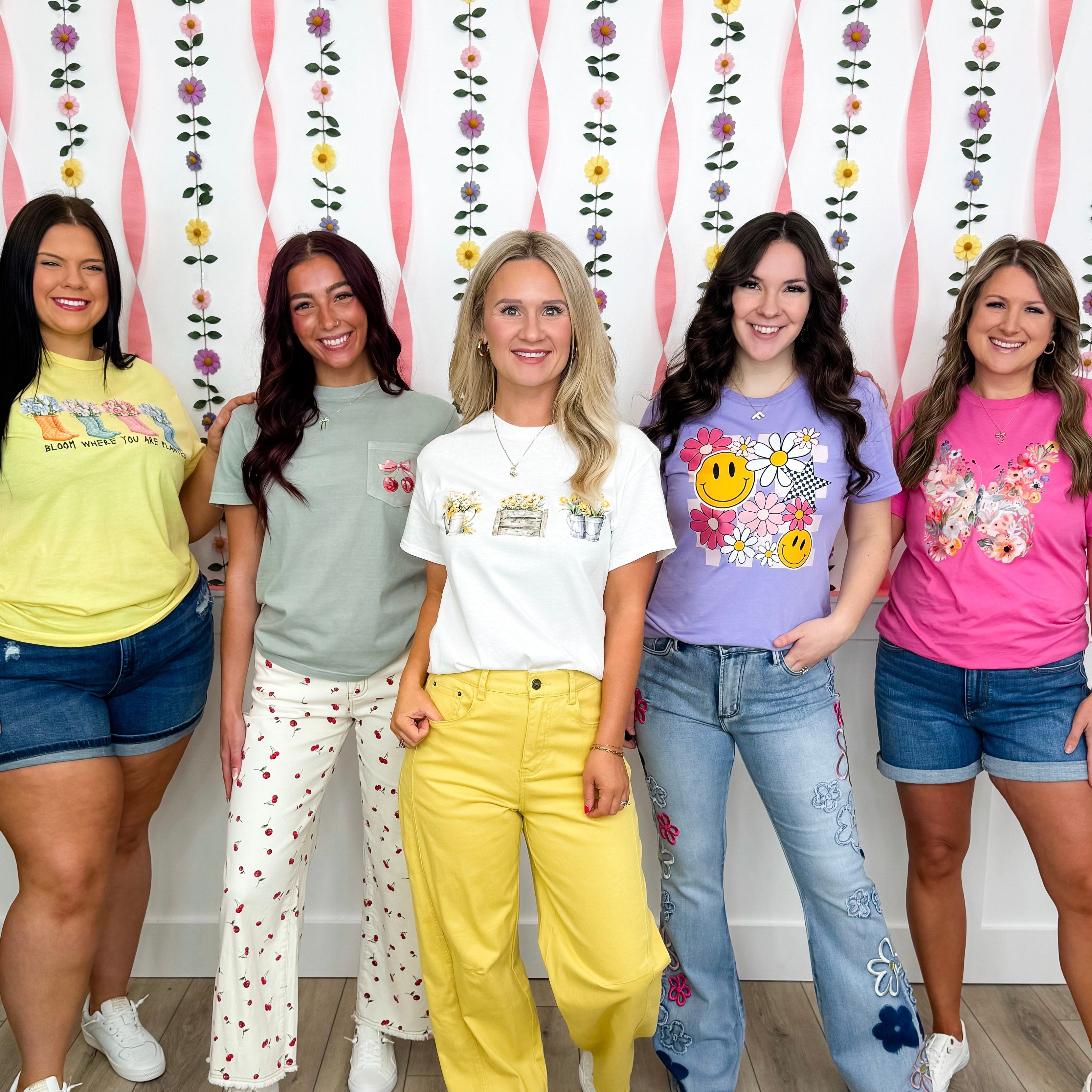 Five women posing together in colorful outfits against a decorative wall.