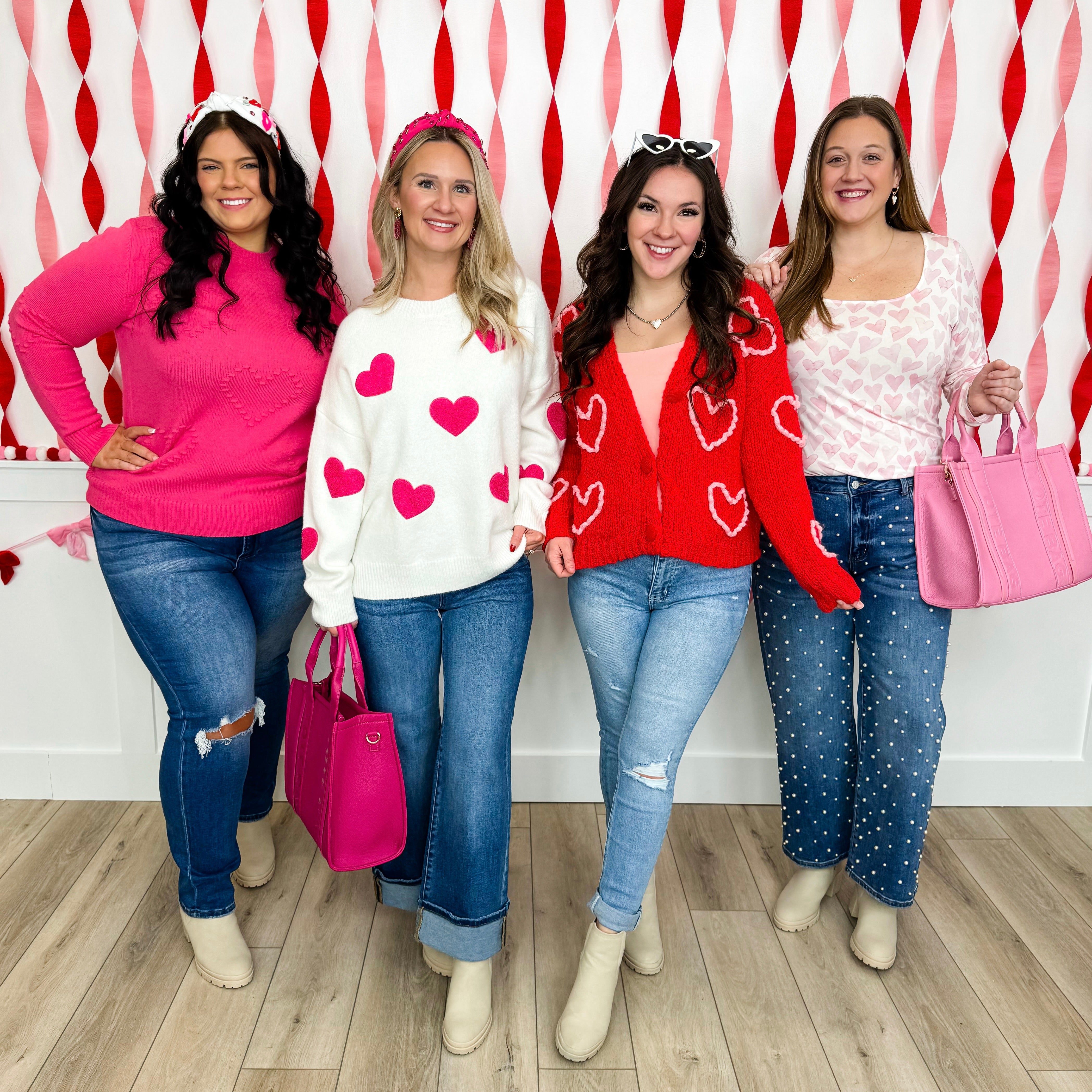 Four women posing together in front of a red and white patterned wall featuring various red pink and white clothing and accessories representing their Valentine's Day Collection.