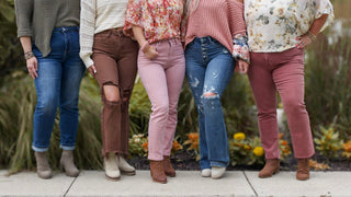Five women shown waist-down in Judy Blue jeans across a range of fits and washes, including blue, brown, blush, and mauve denim, styled with booties at Avery Mae Boutique