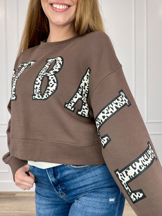 Brown cropped crewneck sweatshirt with leopard-print letter graphics on front and sleeves