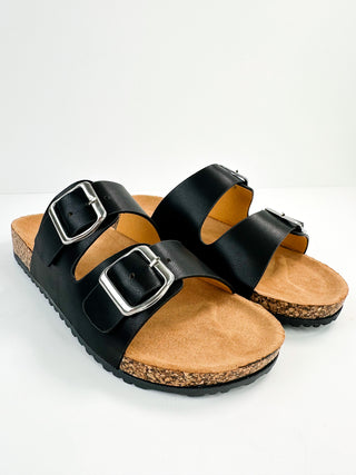 Black faux leather slide sandals with two adjustable buckles, cork-textured sole.