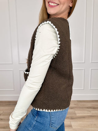 Brown sherpa sleeveless vest with white trim, button front, and side pockets