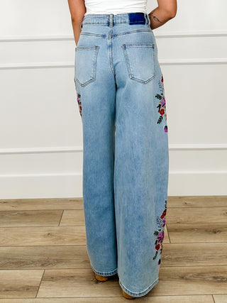 Light wash high-rise wide-leg jeans with floral embroidery on right leg, back view