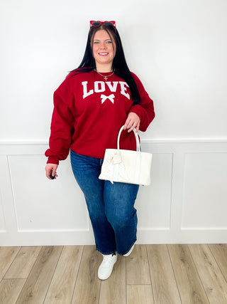 Red sweatshirt with 'LOVE' print, blue jeans, white sneakers, holding white handbag