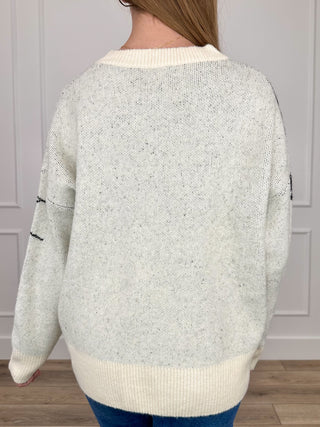Cream knit long-sleeve sweater top with ribbed hem and crew neckline; spiderweb accents