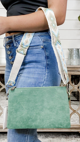 Green suede crossbody bag with patterned shoulder strap and top handle