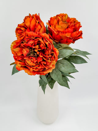 Orange faux peony bundle in white vase with green leaves