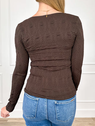 Brown long-sleeve knit top with scoop neck and back gathers, textured floral pattern.