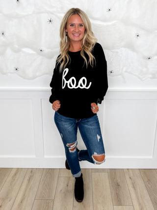 Women's black graphic sweatshirt, distressed blue jeans, and black ankle boots