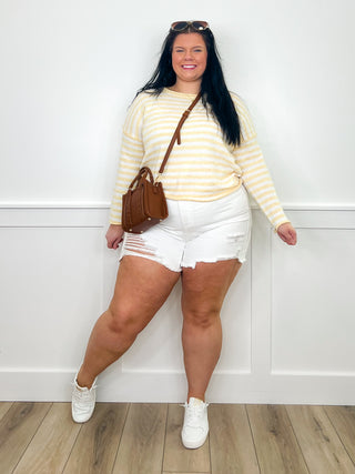 Striped cream sweater, white distressed denim shorts, and white sneakers, with crossbody bag