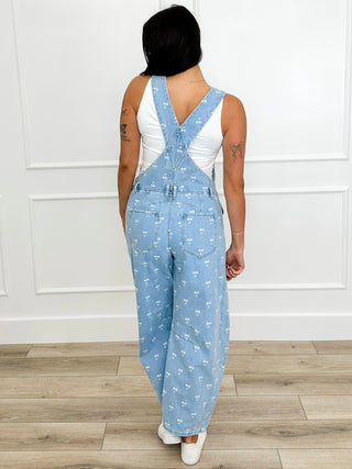 Back view of light blue printed denim overalls with cross-back straps and wide legs