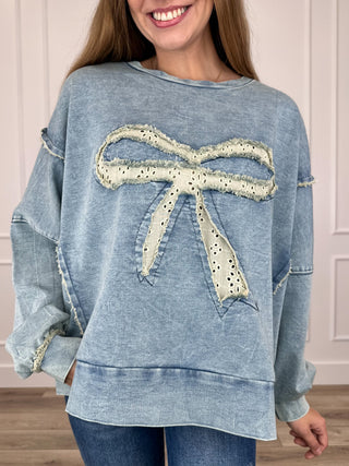 Blue long-sleeve top with distressed neckline and large bow applique on front