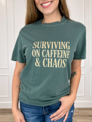 Green short-sleeve crewneck cotton graphic tee with "SURVIVING ON CAFFEINE & CHAOS"