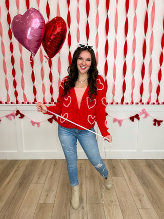 Women’s red heart-pattern sweater, blue jeans, tan boots, sunglasses on head