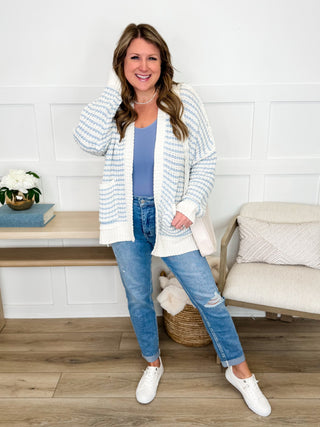 Striped knit cardigan with open front, worn over blue jeans and white sneakers