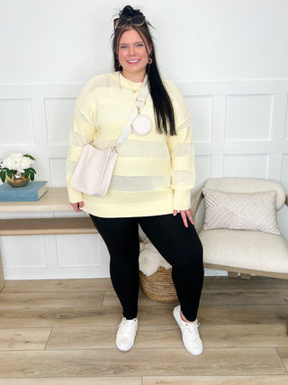 Women's outfit with yellow striped sweater, black leggings, white sneakers, crossbody bag