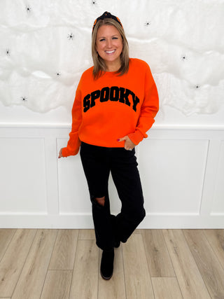 Orange hooded sweatshirt with SPOOKY text and black jogger pants with sneakers