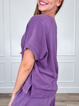 Purple short-sleeve crewneck top shown from side, relaxed draped silhouette