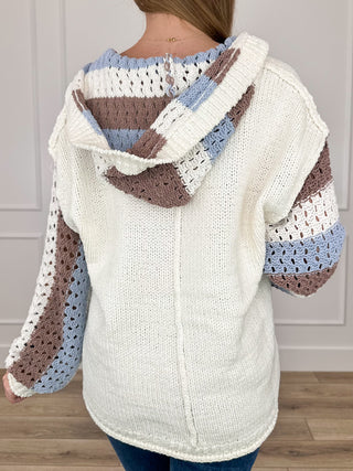 Back view cream knit hooded sweater with blue and brown striped sleeve panels