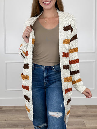 Ivory open-front knit cardigan, long sleeves, bold brown, orange, black stripe pattern.