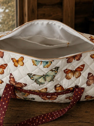 Open quilted ivory duffle bag with butterfly lining and gold zipper, burgundy handle trim