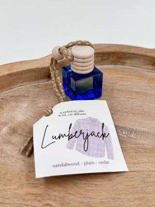 Blue glass scent diffuser bottle with cork cap and braided cord, labeled “Lumberjack”.