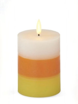 LED pillar candle with layered white top, orange middle band, and yellow base; lit wick
