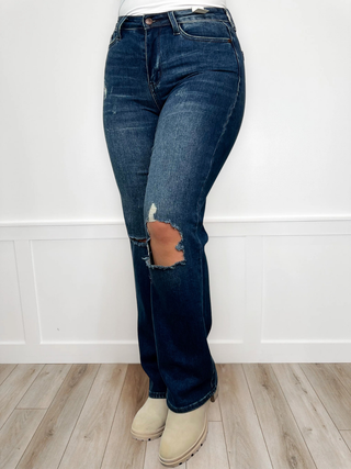 Blue jeans with a distressed knee patch worn by a person on a white background