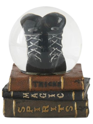 Snow globe with black lace-up boots on stacked spell books, clear dome and base