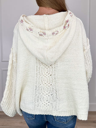 Ivory hooded knit sweater with draped hood and pink/purple stitched tassel accents