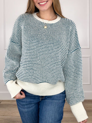 Blue-and-white knit long-sleeve sweater with ribbed cuffs and hem, small button neckline.