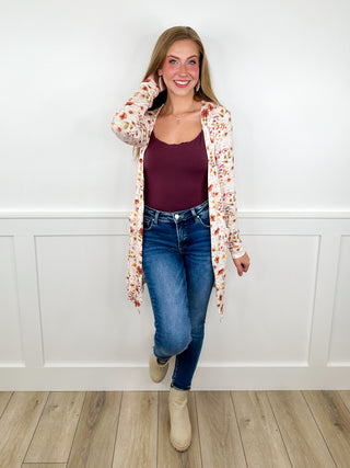 Women’s outfit: floral open cardigan over burgundy top and blue jeans with tan boots