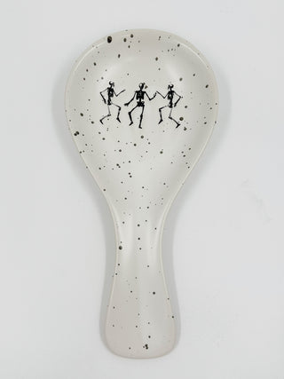 White ceramic spoon rest with speckled finish and black dancing figures