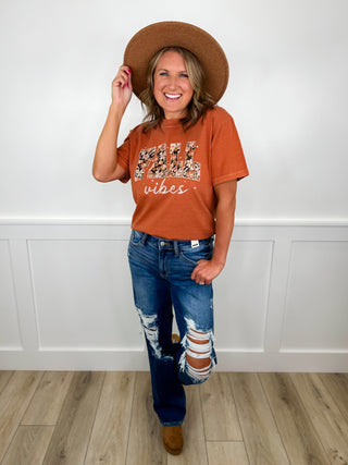 Rust orange graphic T-shirt, ripped blue jeans, brown hat and boots