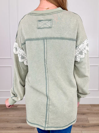 Sage green knit long-sleeve top back with seam lines and white lace-trim cuffs