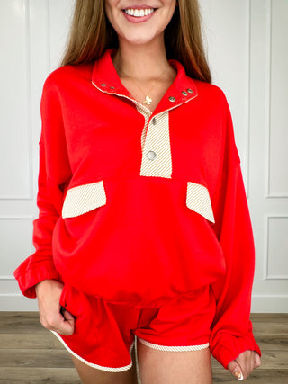 Red long-sleeve pullover top with button placket, patch pockets, and white trim