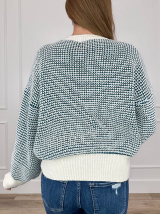 Back view of blue-and-white knit long-sleeve sweater with ribbed hem and neckline button.
