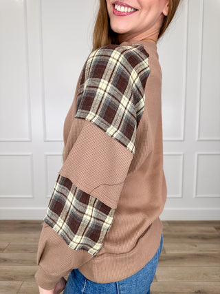 Brown knit long sleeve top, plaid contrast sleeves, relaxed crew neckline.