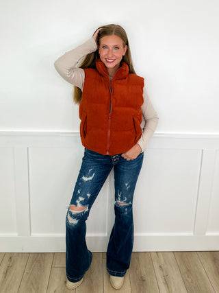 Rust sleeveless puffer vest with zipper and blue distressed jeans, casual outfit