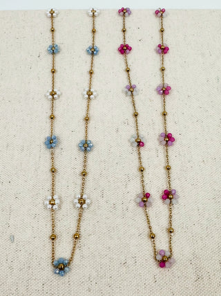 Gold beaded necklace display with blue and purple flower charms on long strands