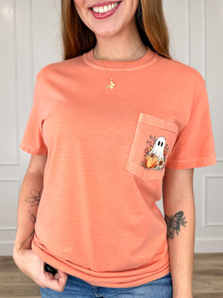 A woman wearing a heathered coral orange short-sleeve pocket t-shirt with a Halloween-themed graphic on the pocket, paired with blue jeans.
