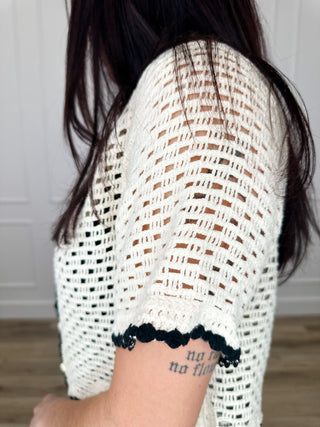 Cream open knit cropped cardigan side view with scalloped dark trim and floral hem applique