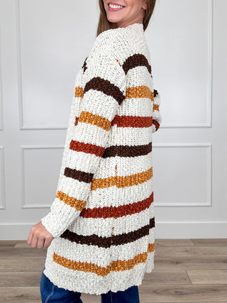 Ivory long knit cardigan with long sleeves and bold brown, orange, black striped pattern.