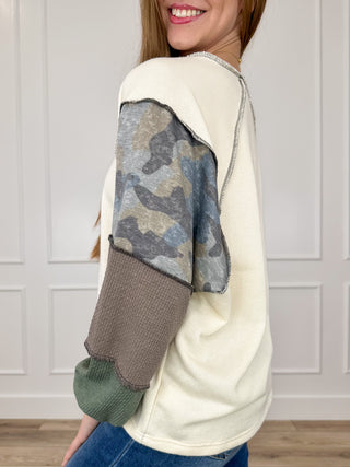 Cream knit long-sleeve top with camo upper sleeves, taupe and green cuffs
