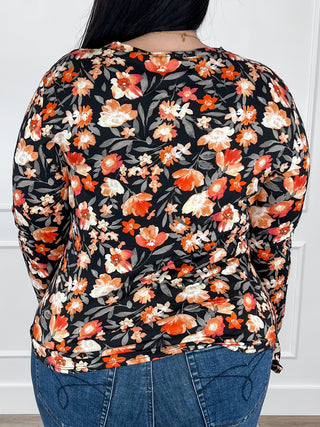 Long-sleeve floral top with black background and orange, white, and cream blossoms