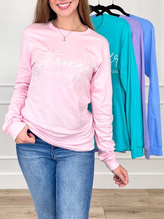 Pink long-sleeve cotton graphic tee with white “Stronger” text; other colors on rack
