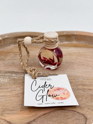 Burgundy glass scent diffuser bottle with cork cap and braided cord, labeled “Cider Glow”.