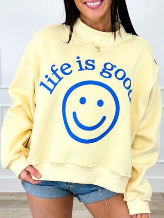 Yellow crewneck long-sleeve top with large blue smiley face and “life is good”